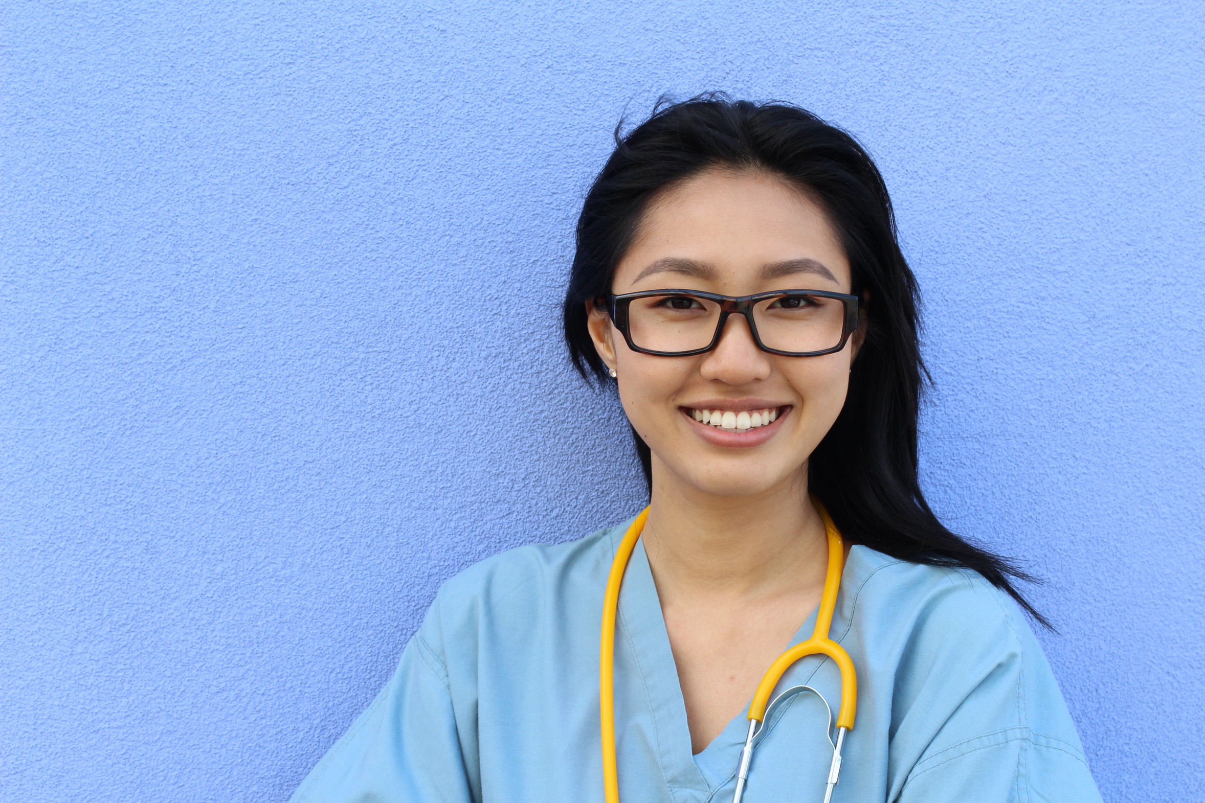 Portrait Of A Confident Mature Female Asian Doctor Looking At Camera Isolated On Blue Background with copy space